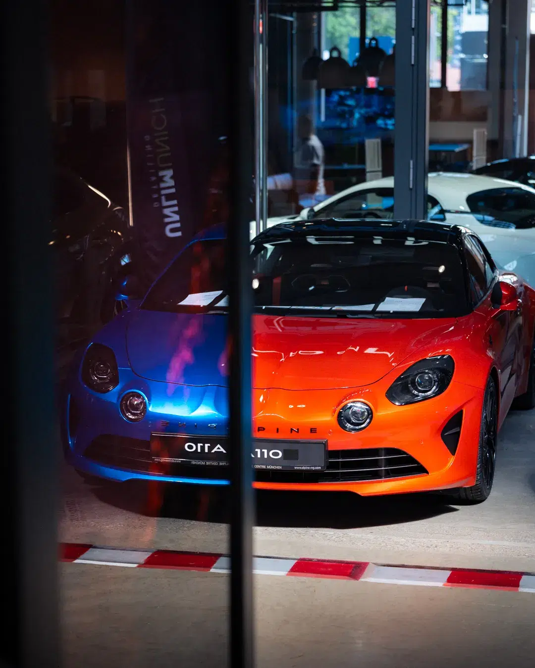 Reflexionen zweier Alpine A110 kreieren Schein eines blau-orangenen A110.